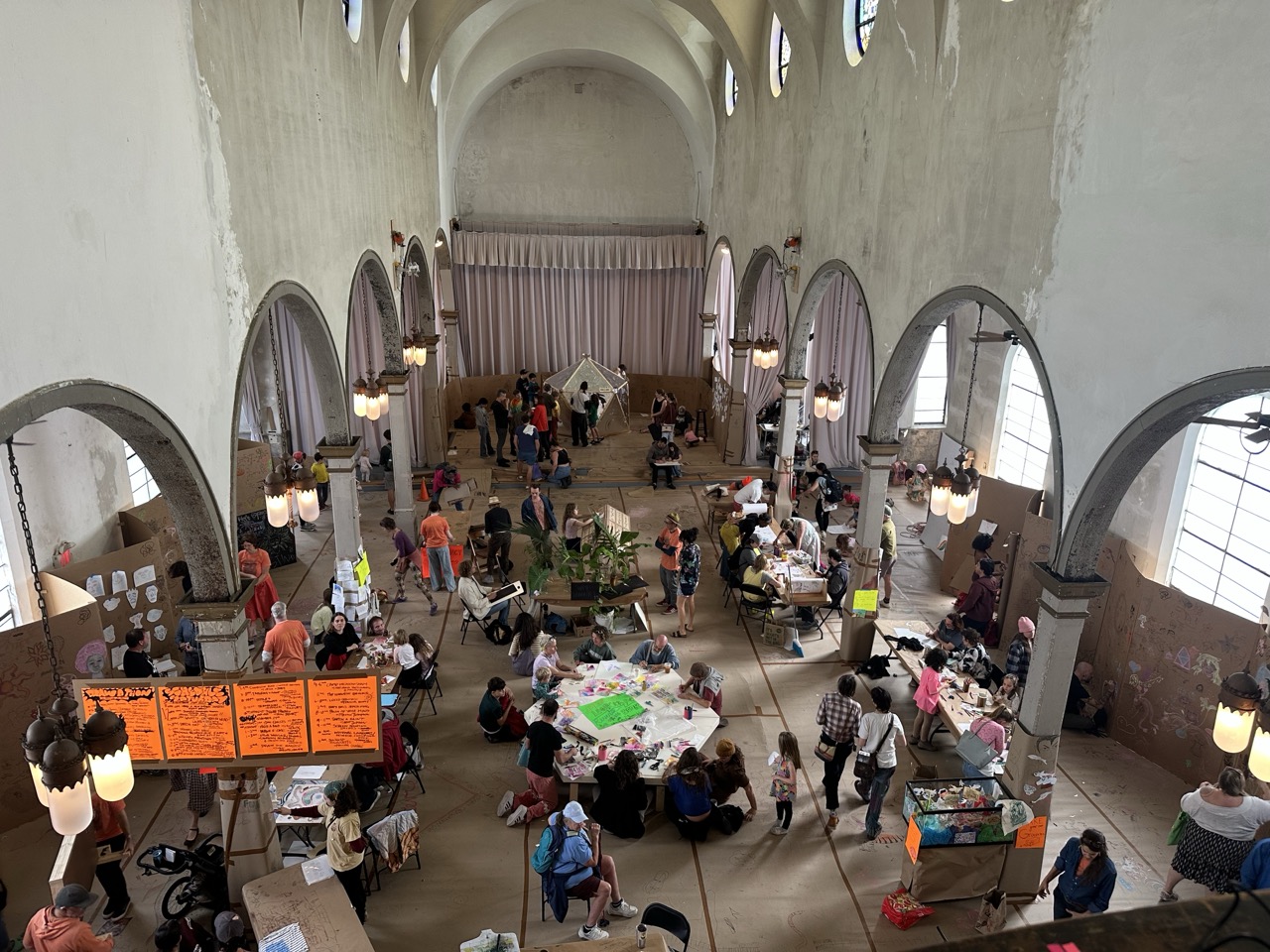 Photo of Drawa-a-thon taken from above at the Marigny Opera House. The space is a former church covered in cardboard. Many people doing workshops.