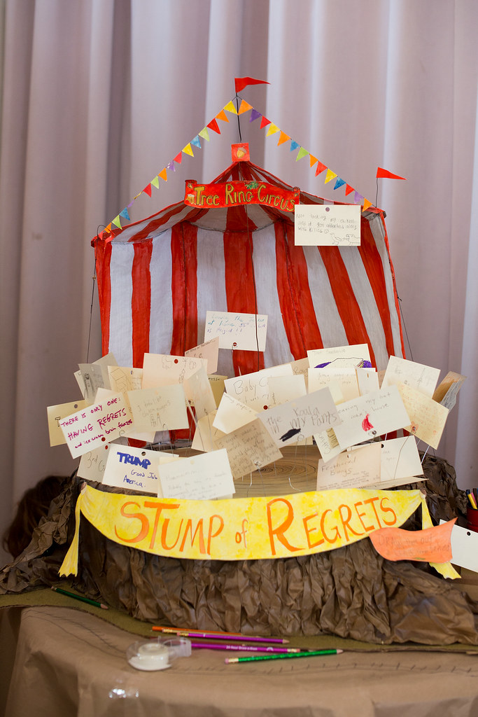“Handmade interactive display shaped like a red-and-white striped circus tent labeled ‘Tree Ring Circus,’ filled with handwritten cards and notes, with a banner reading ‘Stump of Regrets’ and pencils and supplies arranged below.